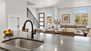 A modern kitchen with a central island, a dining area with a sofa, and a staircase leading to another level. - Desert Beachcomber: Desert Color Lagoon + Beaches (St. George)