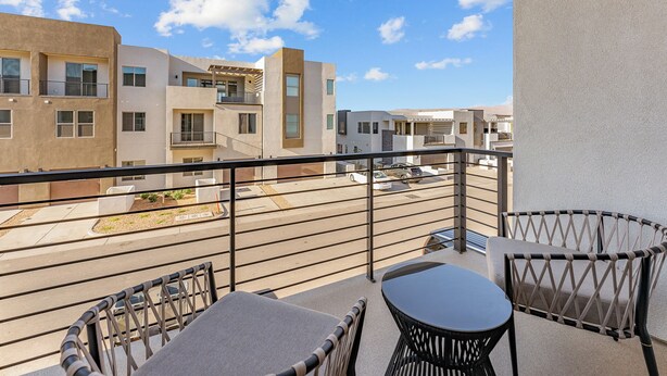A balcony with a table and chairs, overlooking a street with modern buildings and a clear sky. - Desert Beachcomber: Desert Color Lagoon + Beaches (St. George)