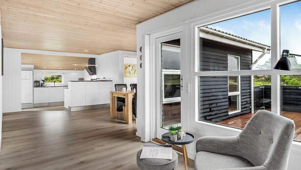 Eine moderne Küche mit weißen Schränken und einer Holzbalkendecke, ein Essbereich mit Tisch und Stühlen sowie ein Blick auf eine Holzterrasse.
