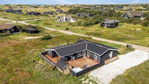 Ein modernes Haus mit einer großen Terrasse, umgeben von einer grünen Landschaft und weiteren Häusern.