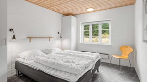 Un dormitorio con cama, una silla, un ventanal y techo de madera.
