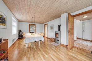 A spacious room with a wooden ceiling, a dining table with chairs, a bookshelf, a fireplace, and a door leading to another room. - Large pool house with activity room located in peaceful surroundings. (Frøstrup)