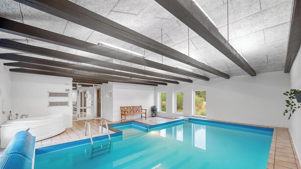 Una piscina interior con un solárium de madera, una banca y vistas al exterior a través de amplias ventanas.