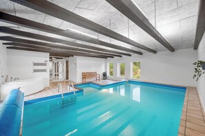 An indoor swimming pool with a wooden deck, a bench, and a view of the outdoors through large windows. - Large pool house with activity room located in peaceful surroundings. (Frøstrup)
