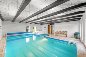 A large indoor swimming pool with a wooden bench and a sauna room in the background. - Large pool house with activity room located in peaceful surroundings. (Frøstrup)