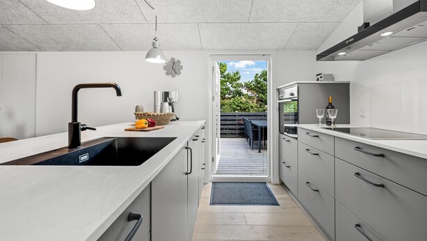 A modern kitchen with a large island, integrated appliances, and a view to an outdoor deck.