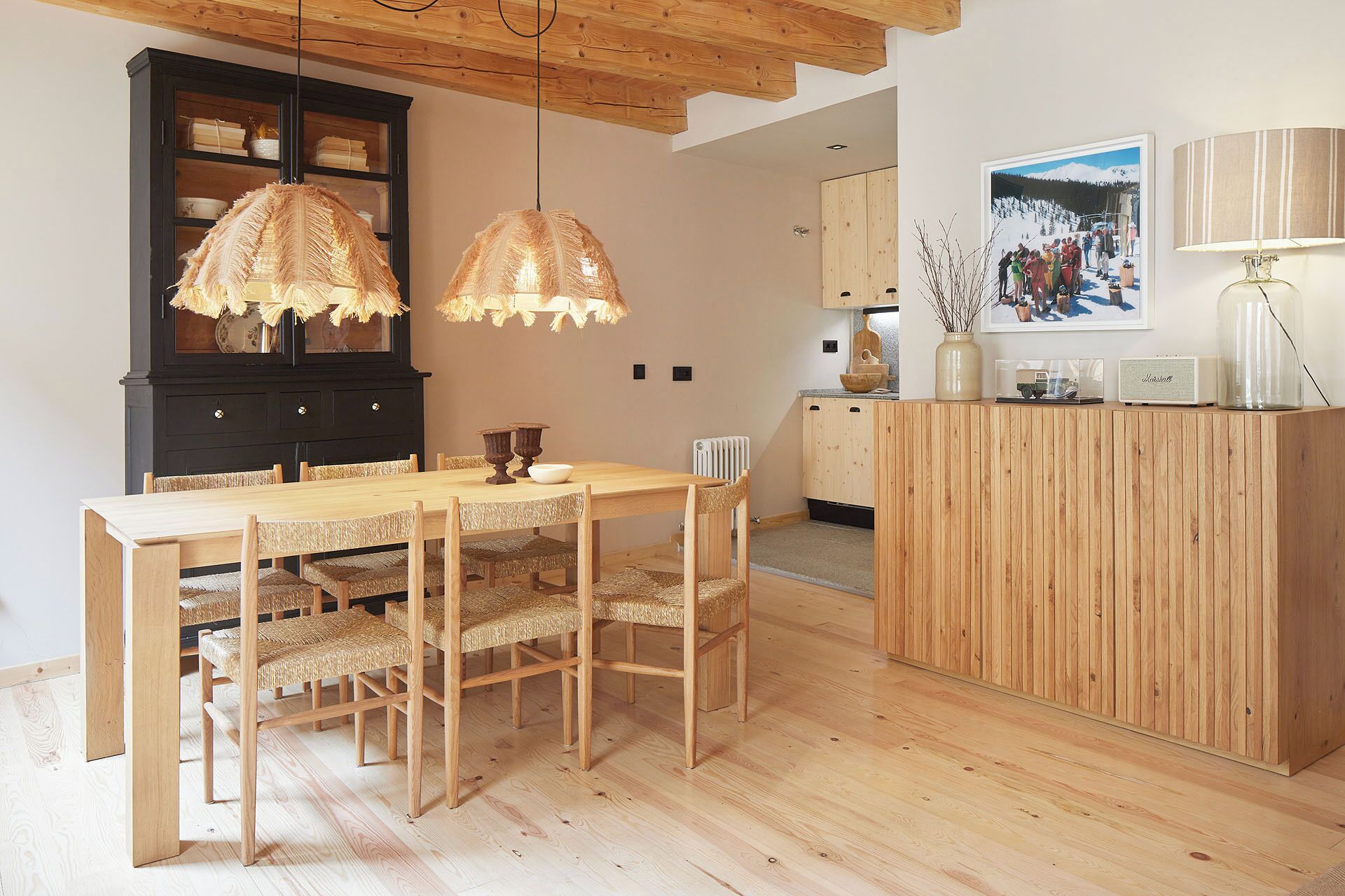 A dining area with a wooden table and chairs, a black cabinet, and a kitchen area with wooden cabinets and a countertop.