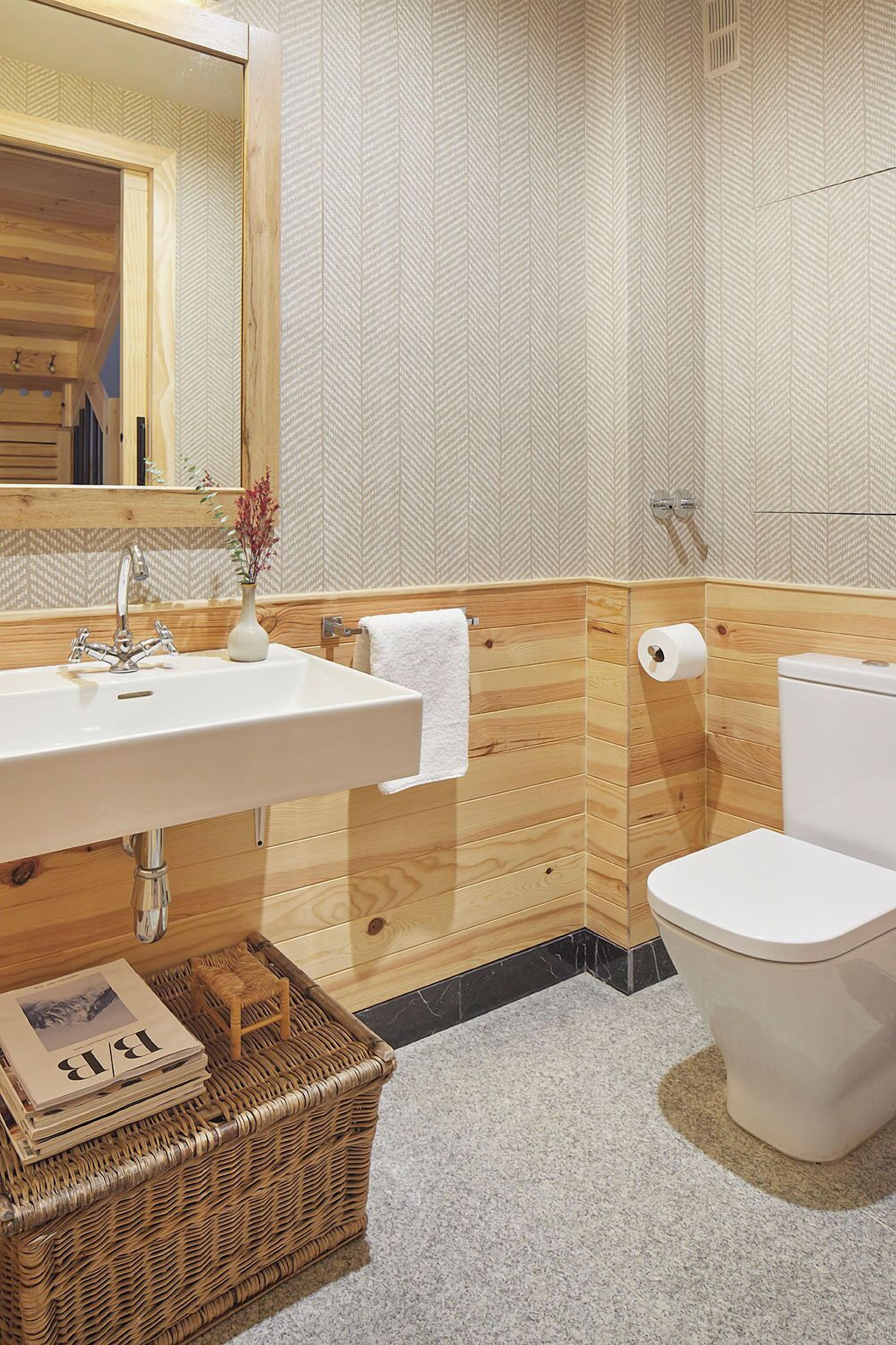 Un baño con tocador de madera, un lavabo blanco, un espejo, un inodoro y un papel tapiz estampado.