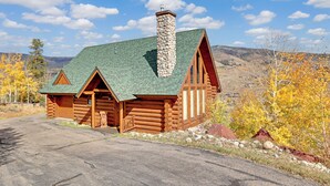 Une cabane en rondins avec une cheminée en pierre, un toit végétalisé et un porche en bois.