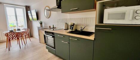 A modern kitchen with dark green cabinets, a built-in oven, a microwave, and a sink.