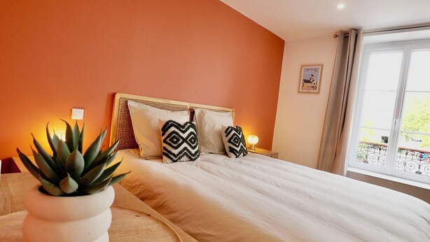 A bedroom with a bed, a bedside table with a plant, and a window with a view. - D-DAY SUITES carentanlocation.fr: TERRA - Downtown / 2-minute walk from the train station (Carentan-les-Marais)