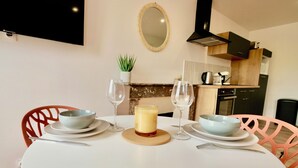 A dining table set with bowls, wine glasses, and a candle. There are chairs around the table, and a kitchen area is visible in the background. - D-DAY SUITES carentanlocation.fr: TERRA - Downtown / 2-minute walk from the train station (Carentan-les-Marais)