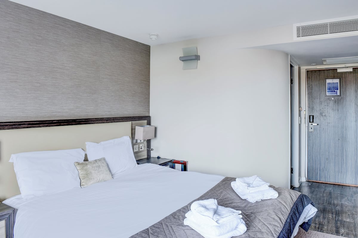 A hotel room with a large bed, a nightstand with a lamp, and a door with a sign.