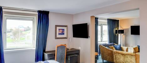 Habitación de hotel con cama, escritorio, silla, televisión y vista al exterior.