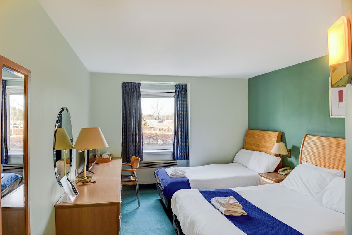 A hotel room with two beds, a desk, a chair, a mirror, and a window with curtains.
