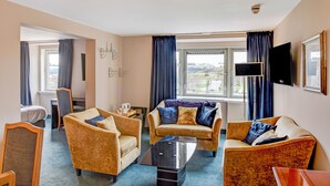 Habitación de hotel con un conjunto de sofá, un televisor de pantalla plana y un ventanal con cortinas.