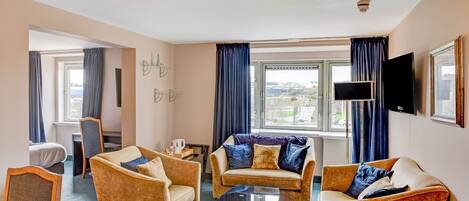 Habitación de hotel con un conjunto de sofá, un televisor de pantalla plana y un ventanal con cortinas.