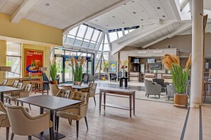 Un vaste espace intérieur doté de hauts plafonds, de grandes fenêtres et de différents types de mobilier, notamment des tables et des chaises.