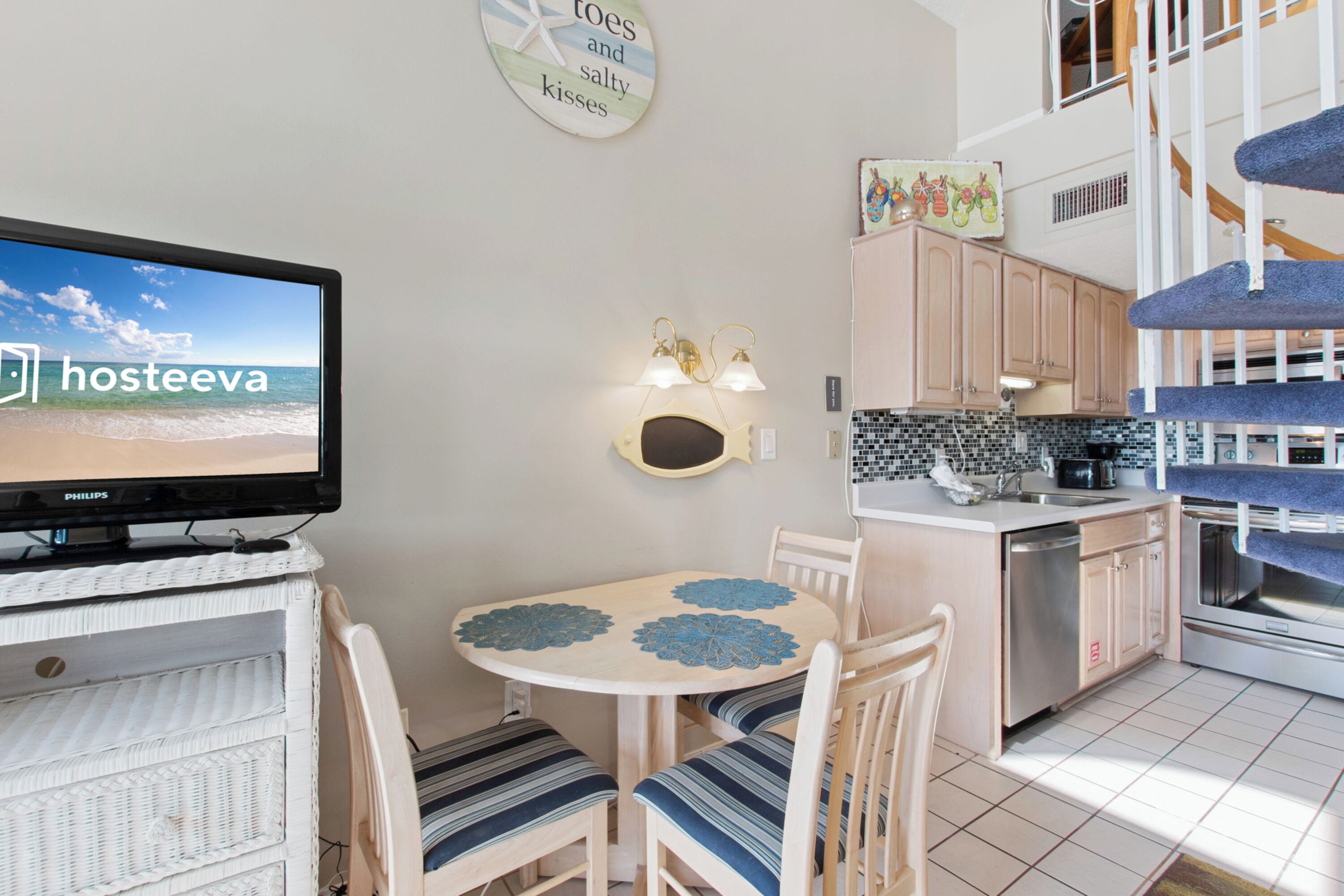A modern kitchen with a dining area, a television, and a staircase.