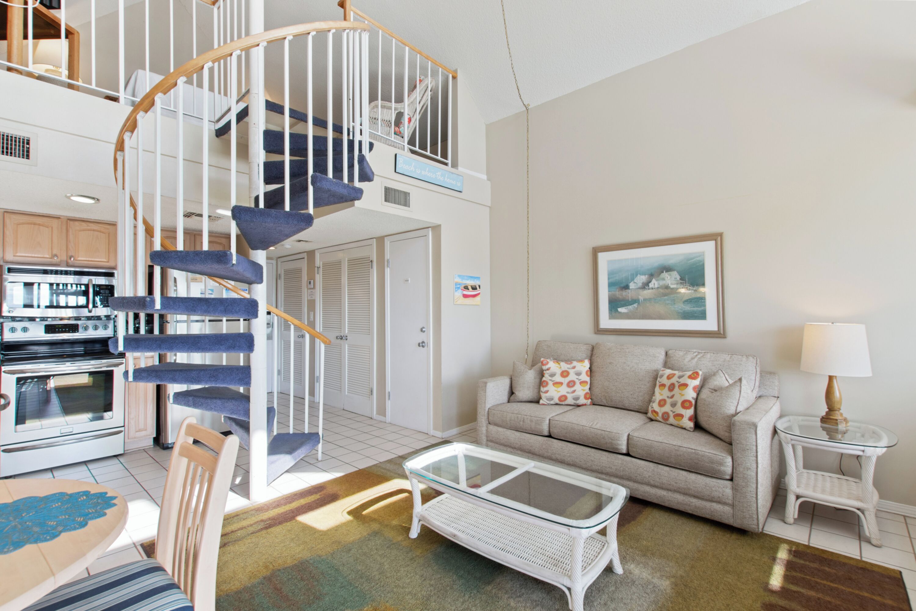 A spacious living room with a spiral staircase, a sofa set, a coffee table, and a kitchen area.