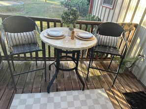 Una terraza de madera con una mesa redonda y dos sillas, una planta pequeña en maceta y un tapete a cuadros.