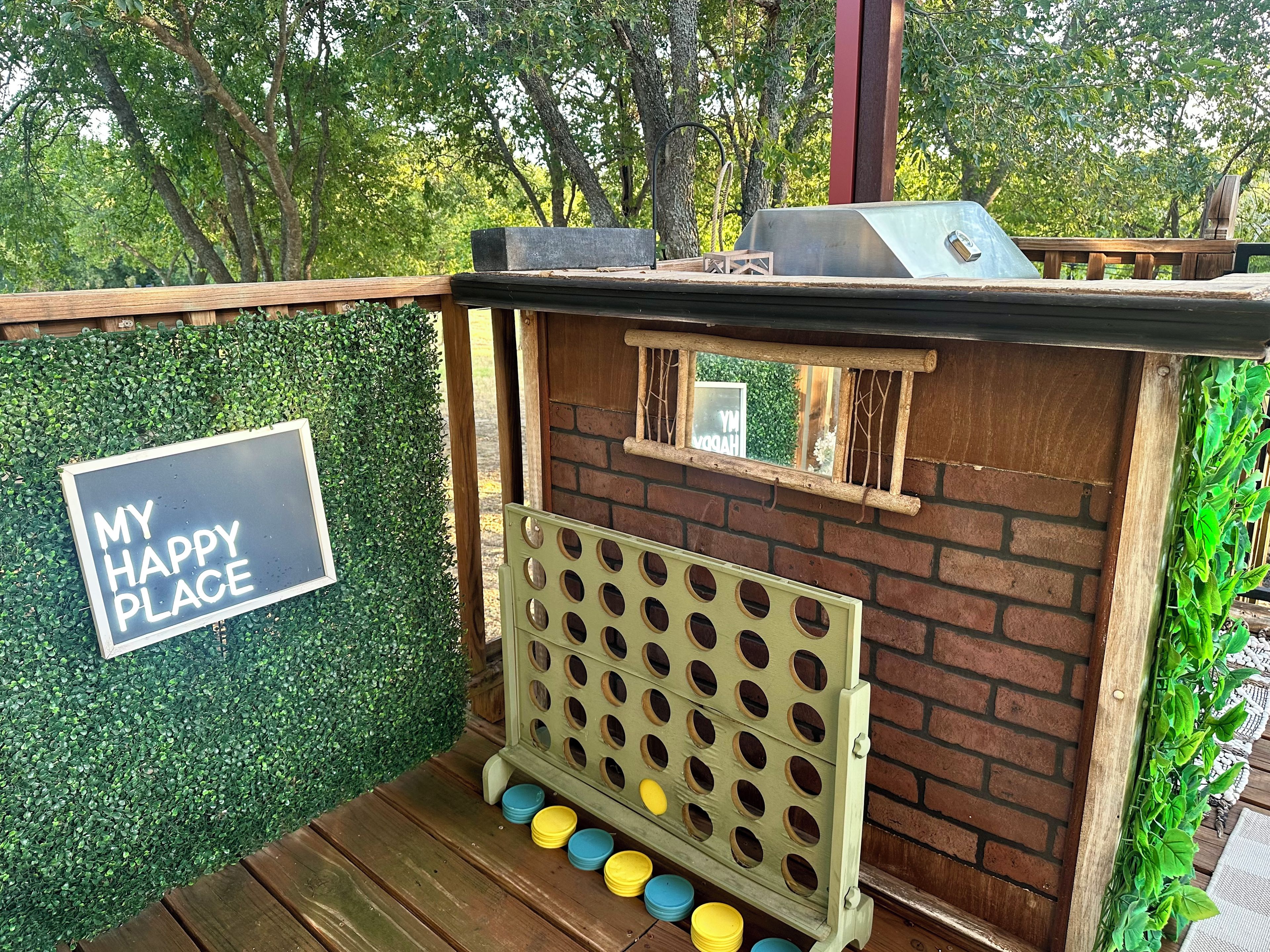 A wooden outdoor structure with a sign that reads 'MY HAPPY PLACE' and a pegboard with colorful buckets.