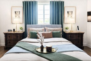 Une chambre à coucher bien rangée, avec un lit, deux tables de chevet, une commode, une fenêtre avec des rideaux et deux lampes fixées au mur.