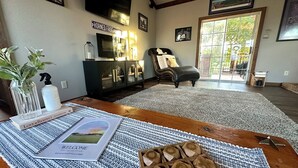 A living room with a wooden coffee table, a rug, a bookshelf, and a television on the wall. - Private Guesthouse in Venus (Venus)