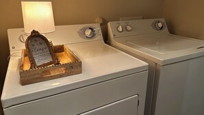 A laundry area with two white washing machines, a wooden tray with a thank you note, and a lamp on the left machine. - Private Guesthouse in Venus (Venus)