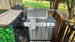 A stainless steel outdoor grill with a control panel, a towel hanging on it, and a patterned rug on a wooden deck. - Private Guesthouse in Venus (Venus)