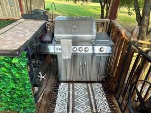 A stainless steel outdoor grill with a control panel, a towel hanging on it, and a patterned rug on a wooden deck. - Private Guesthouse in Venus (Venus)