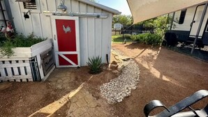 A small shed with a red door, a white fence, and a patio area with a grill and outdoor seating. - Private Guesthouse in Venus (Venus)