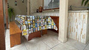 A kitchen with a tiled floor, a wooden bench, a table covered with beer cans, a window, and a sink. - Oásis Morro das Pedras - Floripa (Florianópolis)
