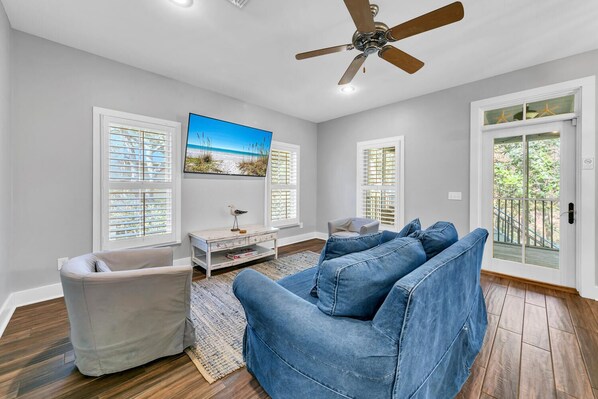 A spacious living room with a ceiling fan, a large TV, and a view of the outdoors through a sliding glass door.