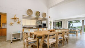 Un vaste espace de salle à manger avec une table et des chaises en bois, une cuisine à l’arrière-plan et un balcon avec vue.