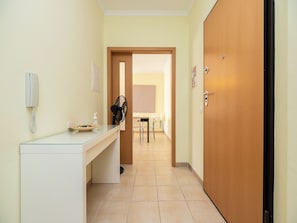A hotel reception area with a reception desk, a telephone, a fan, and a door leading to a dining area.