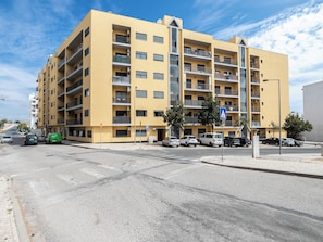 Un edificio amarillo de varios pisos con balcones, una señal de estacionamiento y varios autos estacionados adelante.
