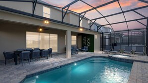 Zona de piscina con techo de cristal, mobiliario exterior y vistas al atardecer.