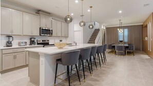 Una cocina moderna con armarios blancos, una isla central con taburetes y electrodomésticos como microondas y cafetera.