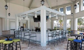 An outdoor bar area with a white column structure, multiple bar stools, and a television screen. - Amazing 5Bdrms At Storey Lake (Kissimmee)
