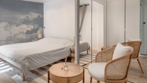 A modern hotel room with a large bed, two wicker chairs, a round wooden table, and a world map on the wall.