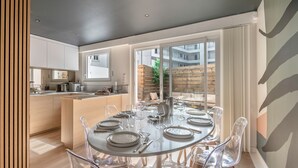 A modern kitchen with white cabinets, a dining area with a round table set for six, and a view of a balcony with a wooden fence.