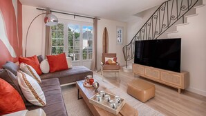 A modern living room with a sofa, a coffee table with cups, a TV, and a staircase.