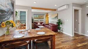 A dining area with a wooden table set for two, a red leather sofa, and a large abstract painting on the wall.