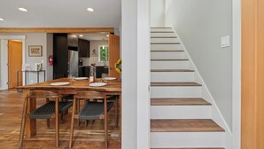 A modern kitchen with dark cabinetry, a wooden dining table, and a staircase with wooden steps.