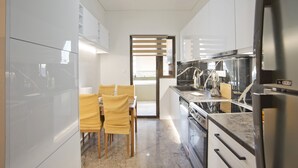 A modern kitchen with white cabinets, a marble countertop, and a built-in oven. There is a dining area with yellow chairs and a table. - Afrodite Classic Residence, 2BR, WiFi, City View (Paleo Faliro)
