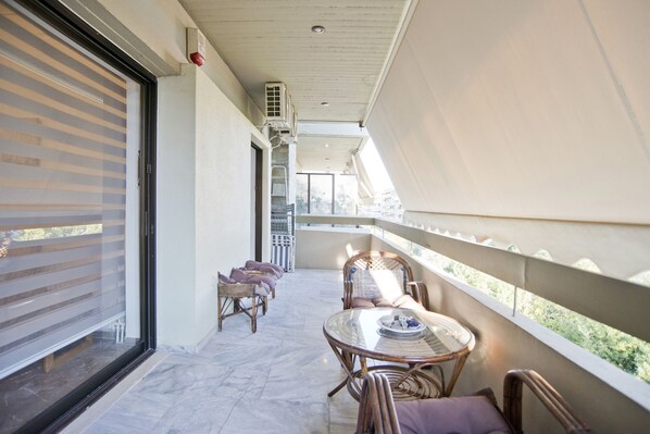 A balcony with wicker chairs, a glass table, and a view of the outdoors. - Afrodite Classic Residence, 2BR, WiFi, City View (Paleo Faliro)
