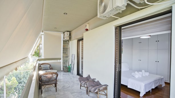 A balcony with wicker furniture, a bed with white linens, and a view of greenery. - Afrodite Classic Residence, 2BR, WiFi, City View (Paleo Faliro)