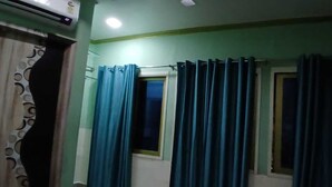 A room with teal walls, a window with curtains, and an air conditioning unit. - Rudraksh Home Stay (Varanasi)