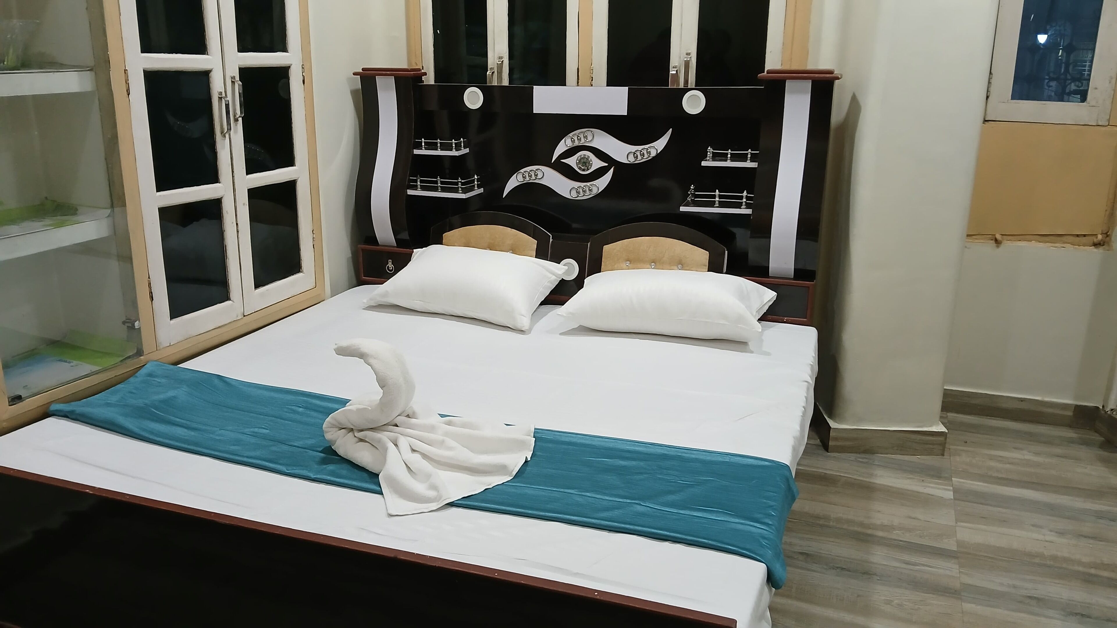 Une chambre d’hôtel avec un lit, deux oreillers, une tête de lit décorative et une fenêtre avec des stores.